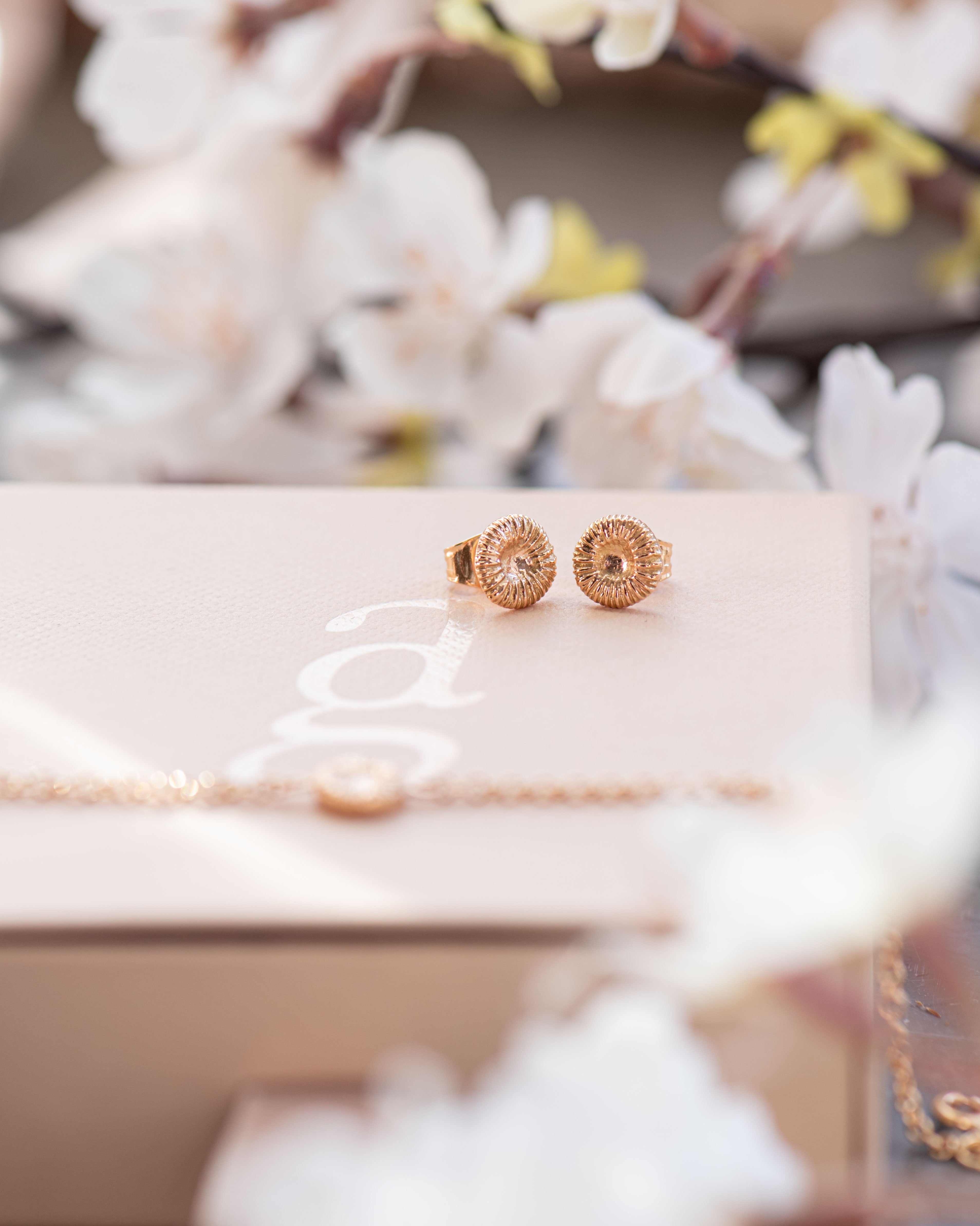 Guldfärgade örhängen på en beige ask med blommor i bakgrunden.